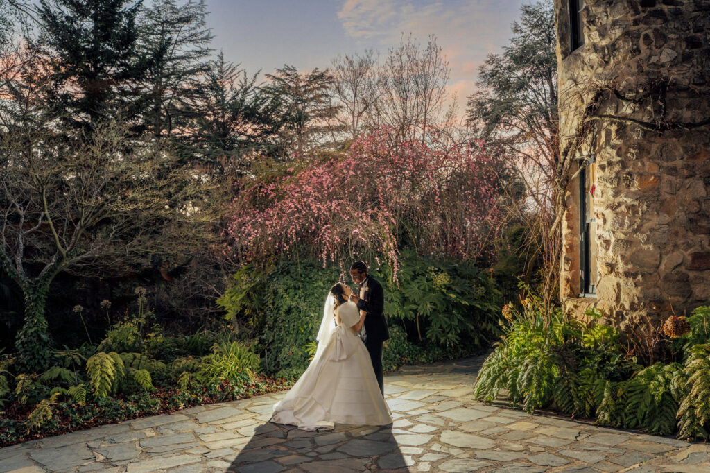 Bride Karen and groom George standing under a pink blossom tree at dusk in the gardens of The Manor Basket Range.